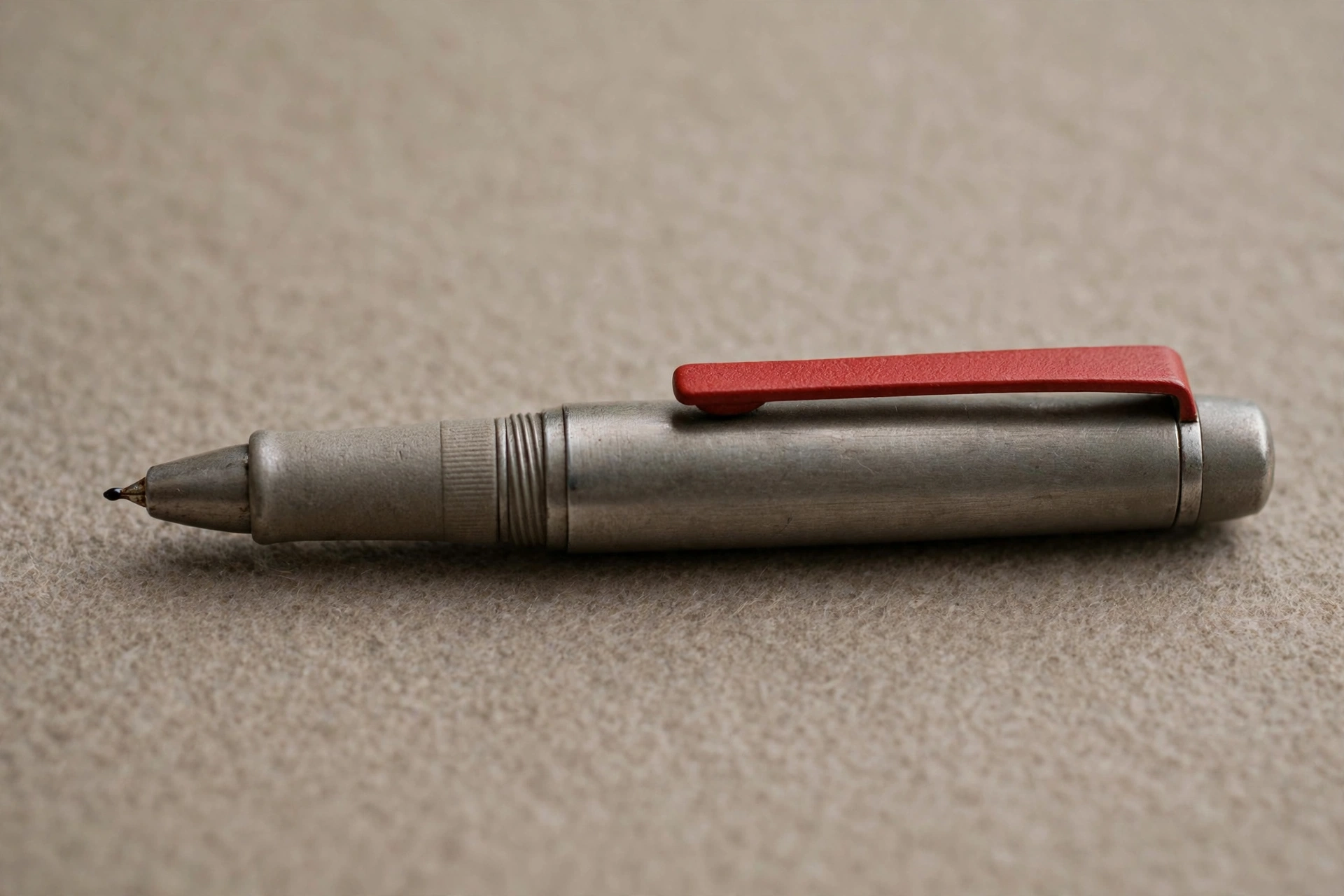 A photograph of a silver pen with a red clip resting on a beige surface.