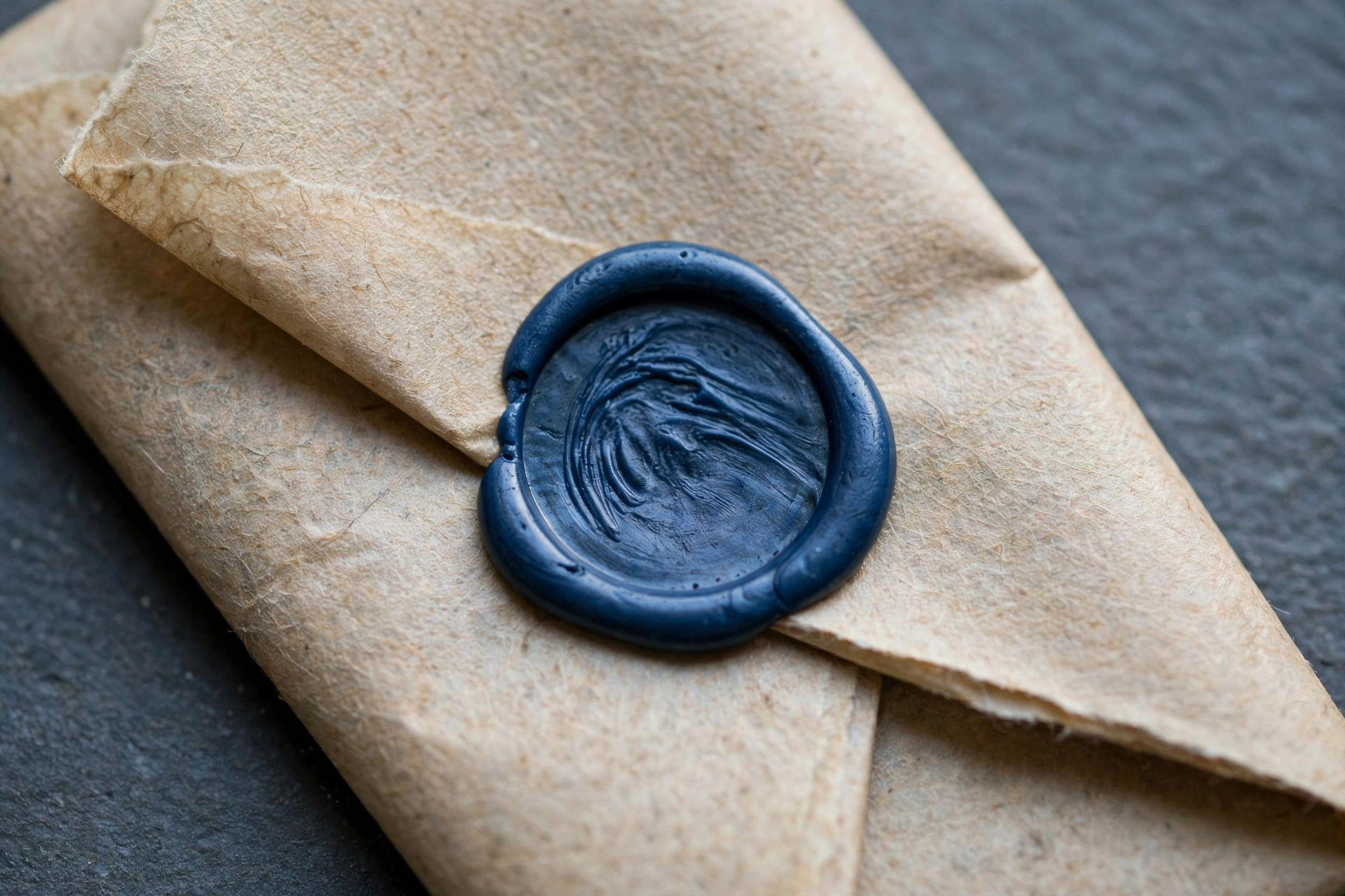 A photograph of a dark blue wax seal on a tan paper envelope.