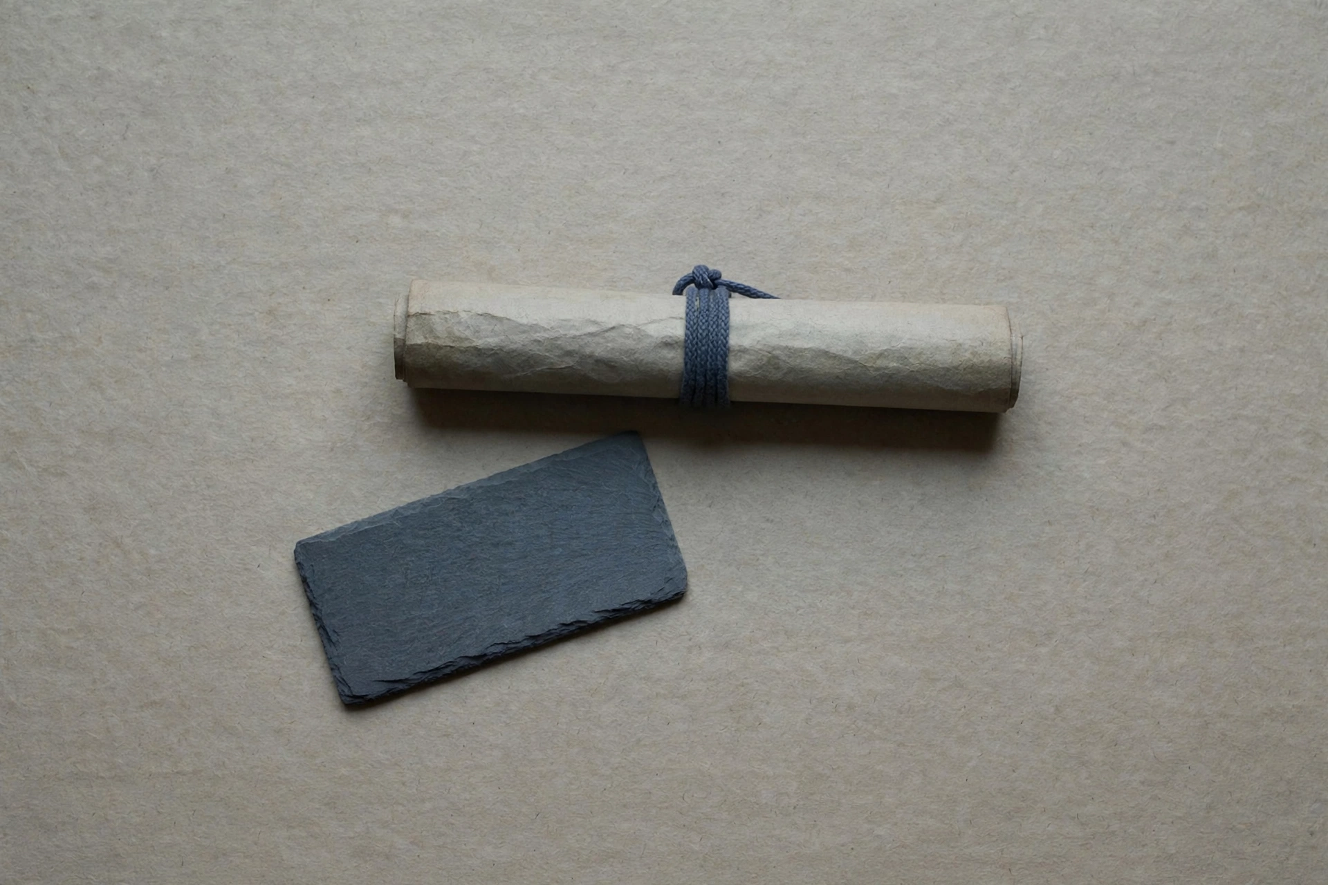 A photograph of a rolled-up scroll tied with blue string and a dark slate rectangle.