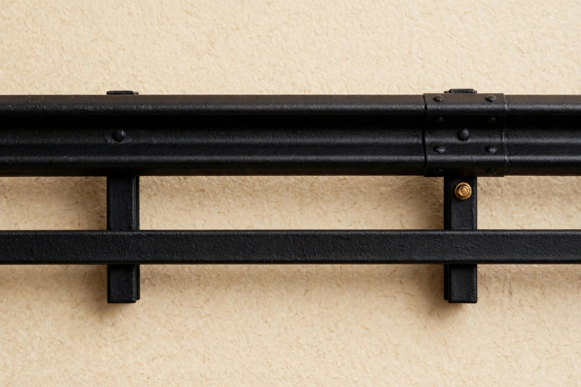 A photograph shows a section of a black metal guardrail attached to a textured cream-colored wall.