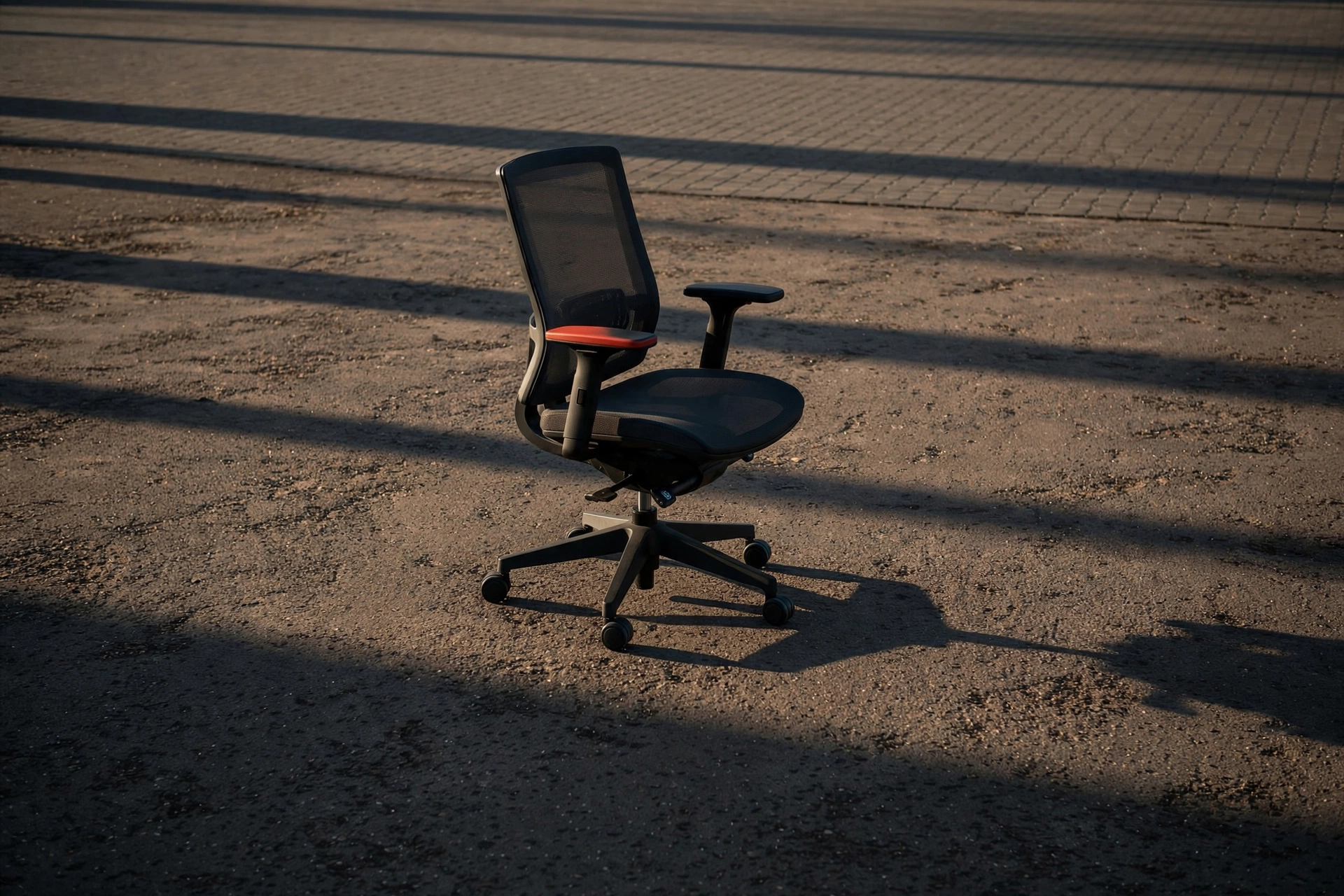 A photograph shows a black office chair with a red accent on a paved surface.