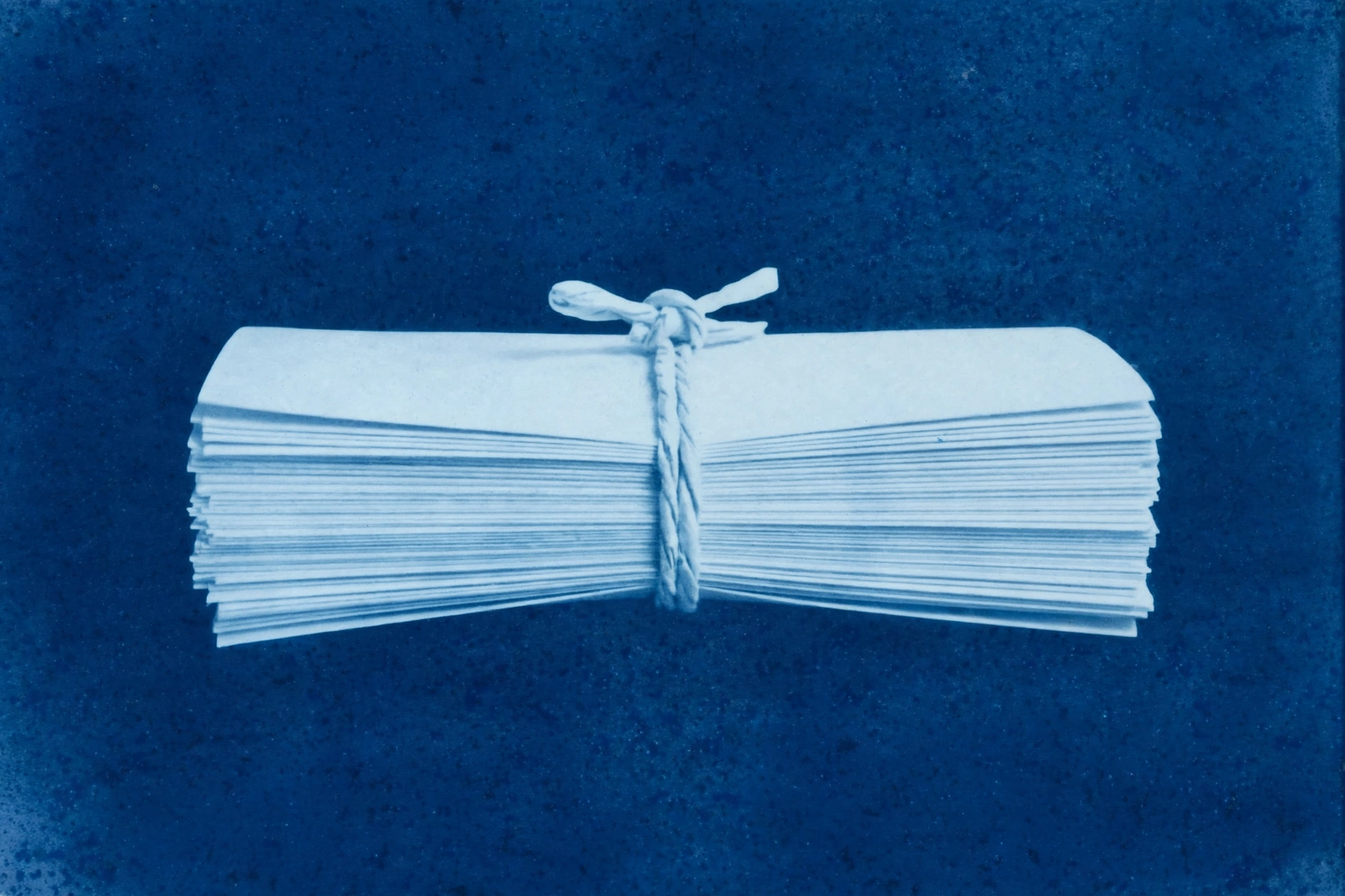A cyanotype photograph of a stack of folded papers tied with twine.