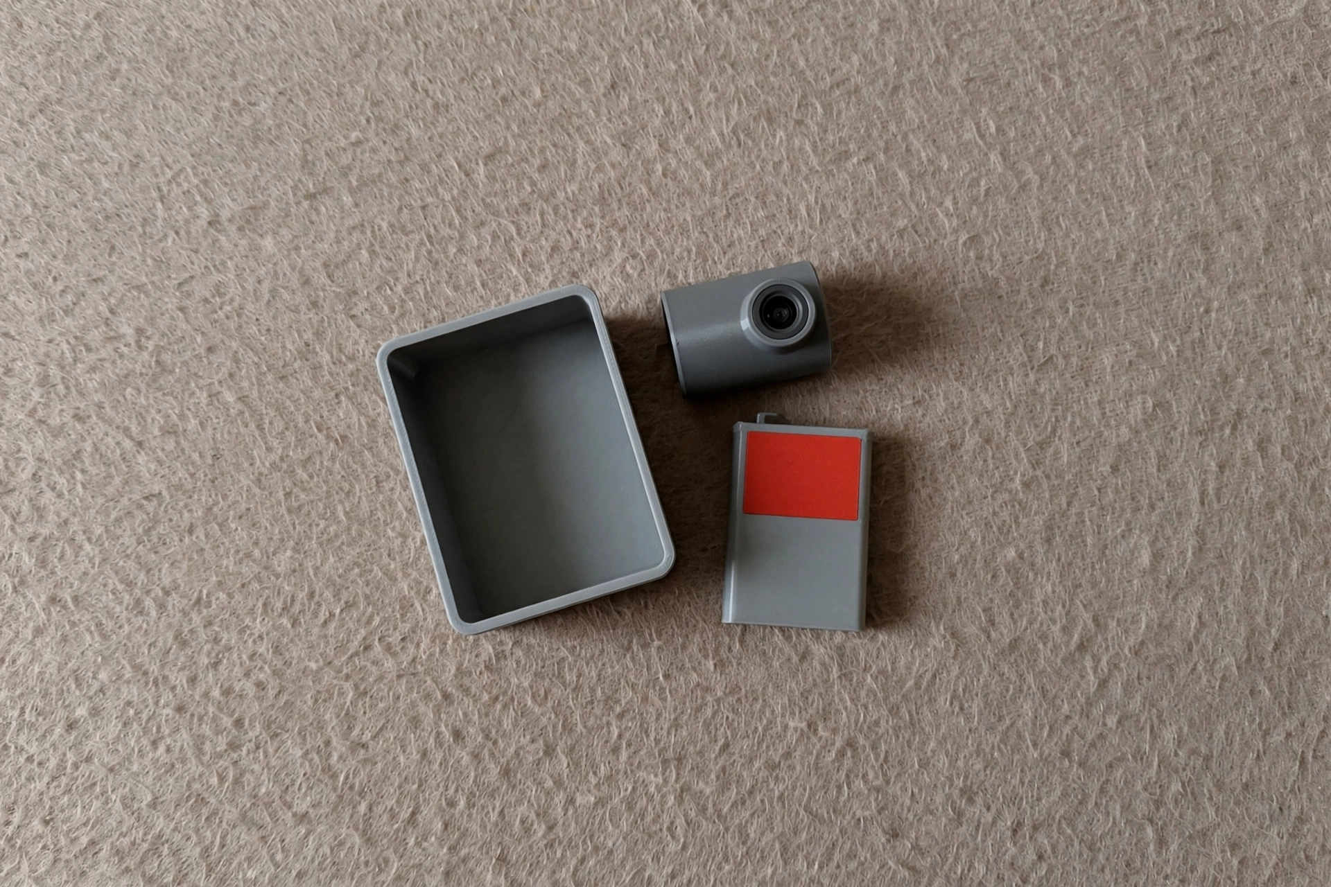 A photograph shows a grey container, a grey camera, and a grey battery with a red rectangle on it.