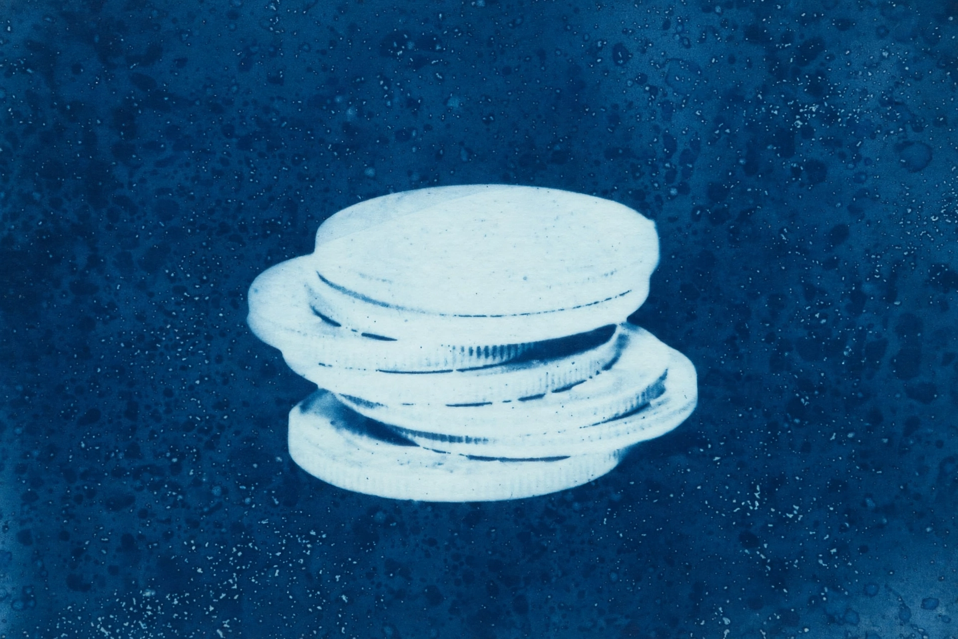A cyanotype photograph shows a stack of coins.