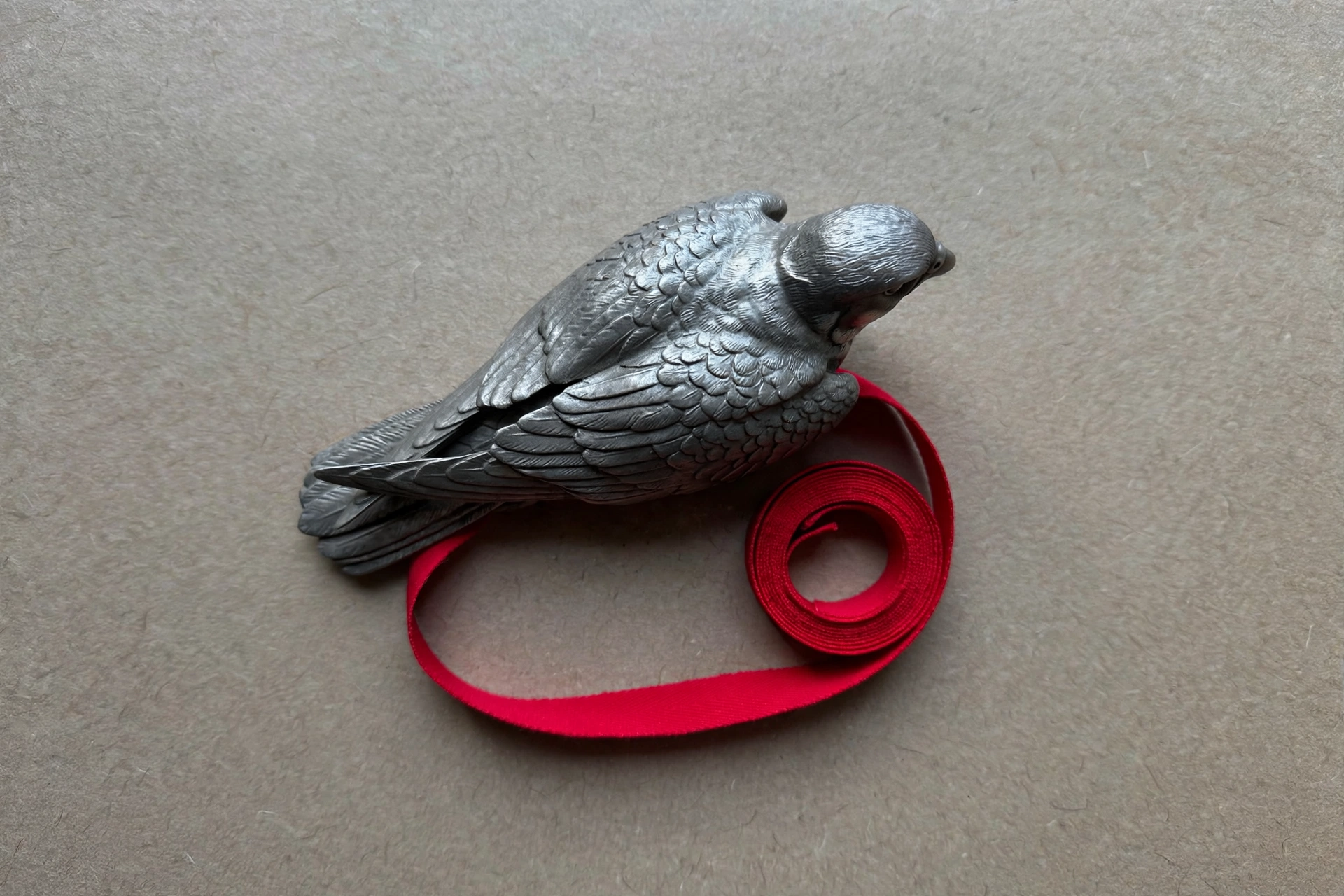 A photograph of a metal bird figurine resting on a red ribbon.