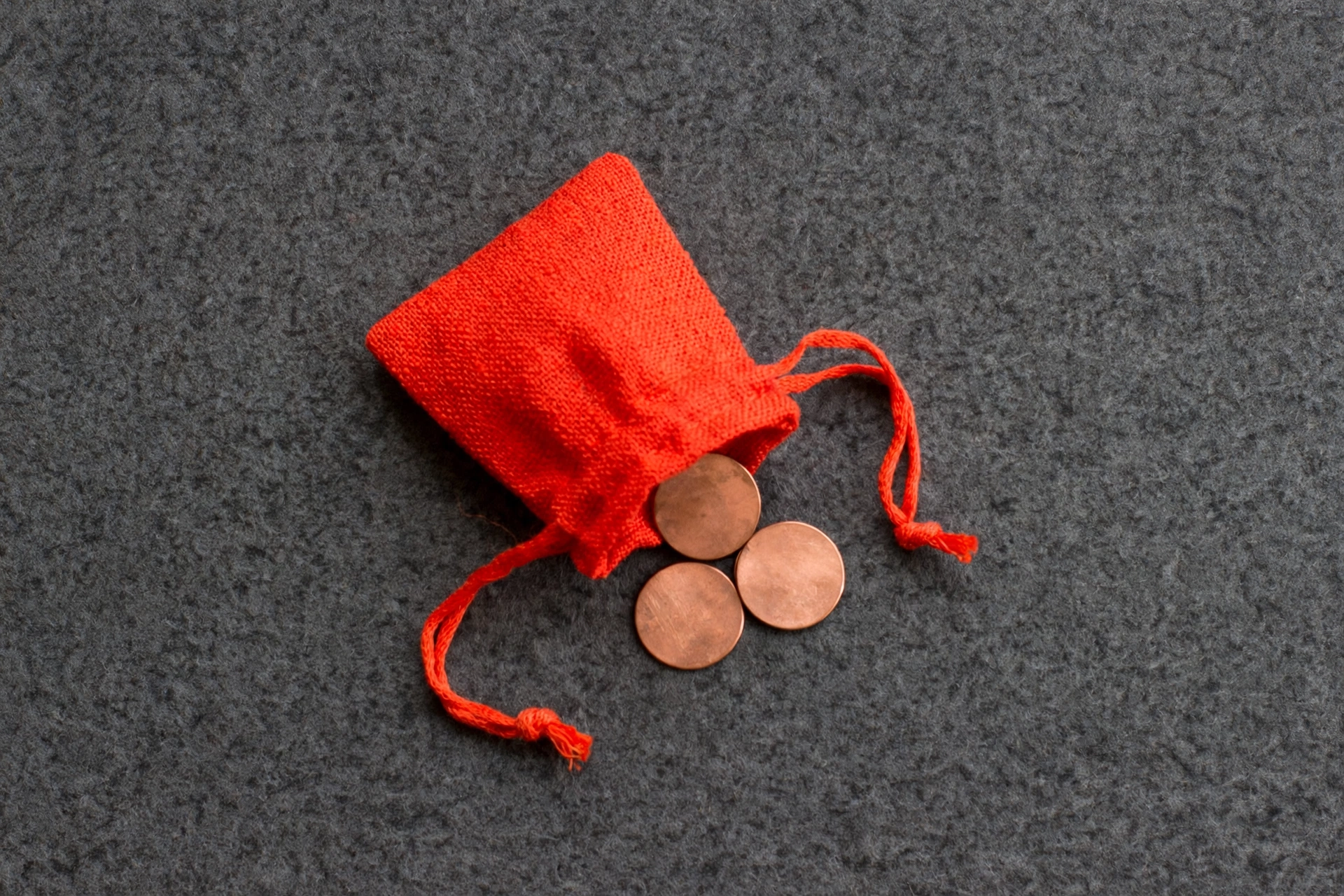 A photograph shows an overturned red drawstring bag with three copper coins spilling onto a gray textured surface.