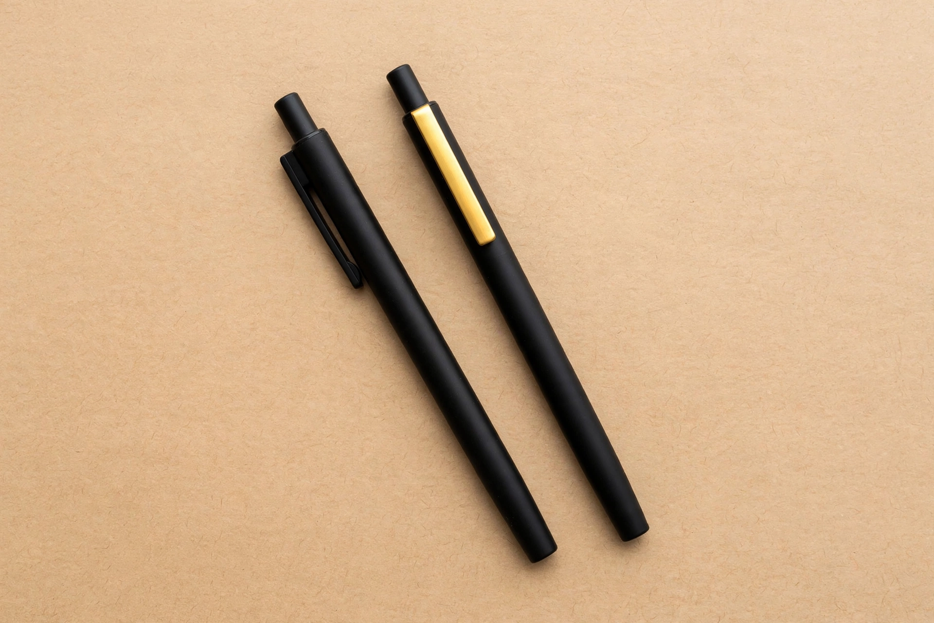 A photograph shows two black pens lying diagonally on a tan background.
