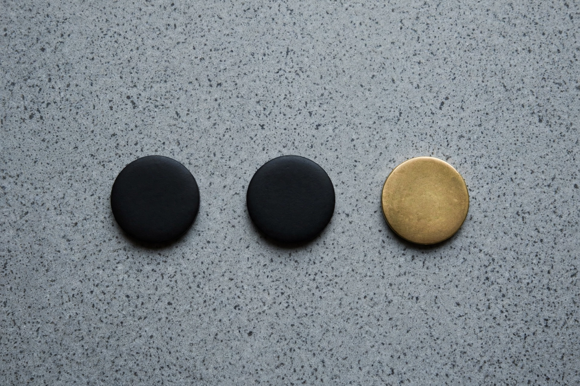 A photograph of three round objects on a speckled grey surface, two are black and one is gold.