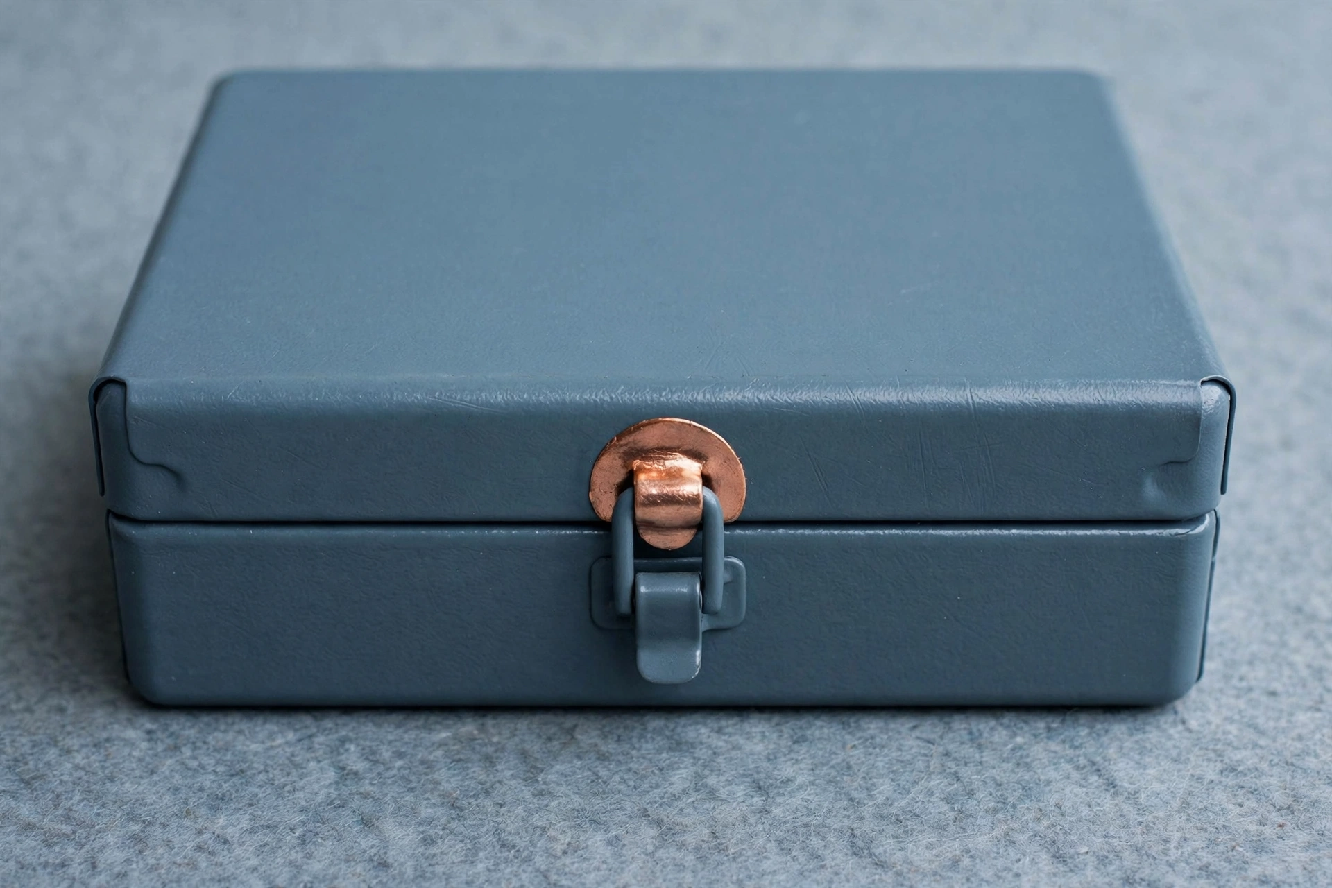 A photograph of a closed, blue, rectangular metal box with a copper latch.