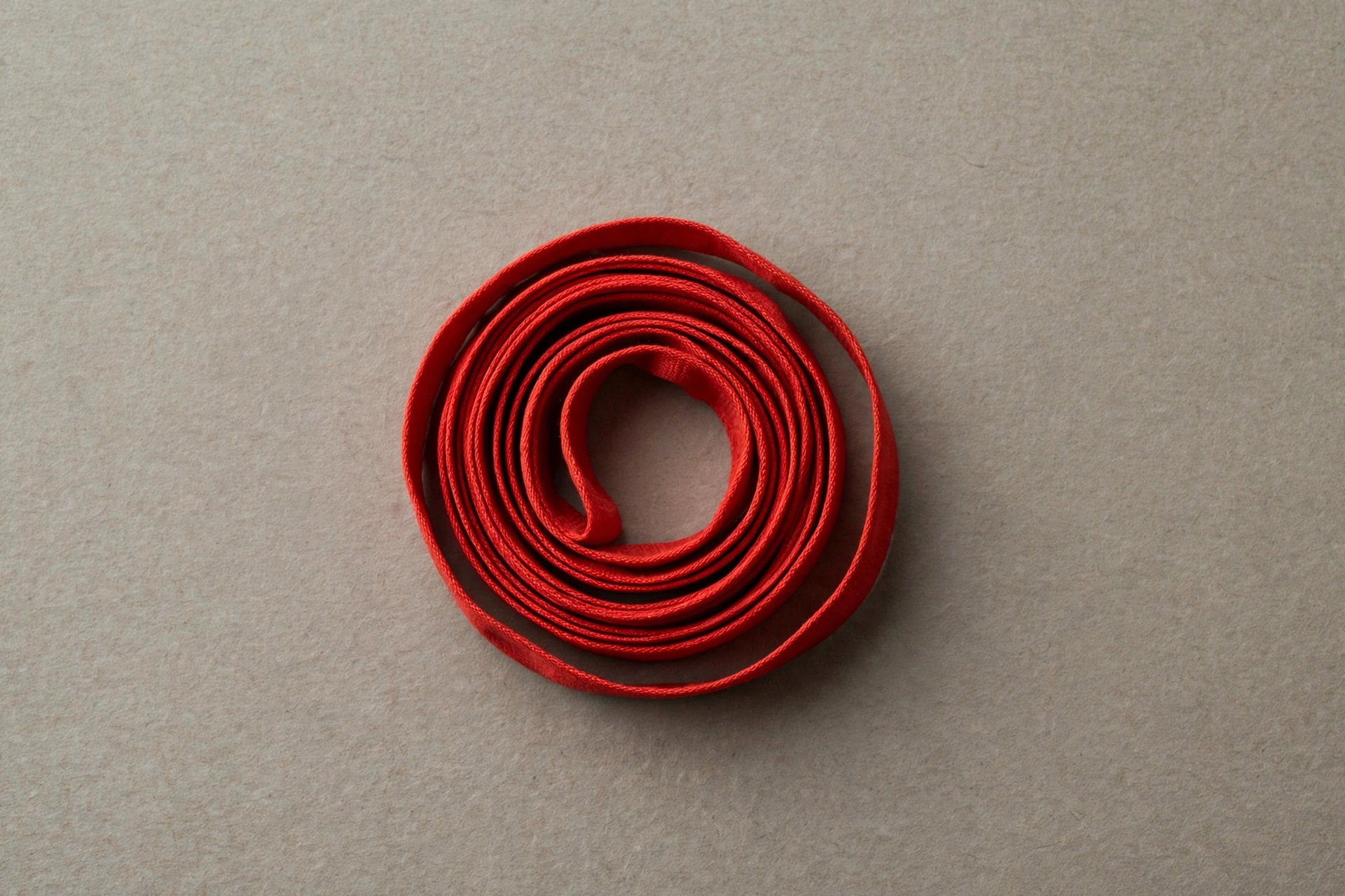 A photograph of a tightly rolled loop of red satin ribbon on a plain gray background.