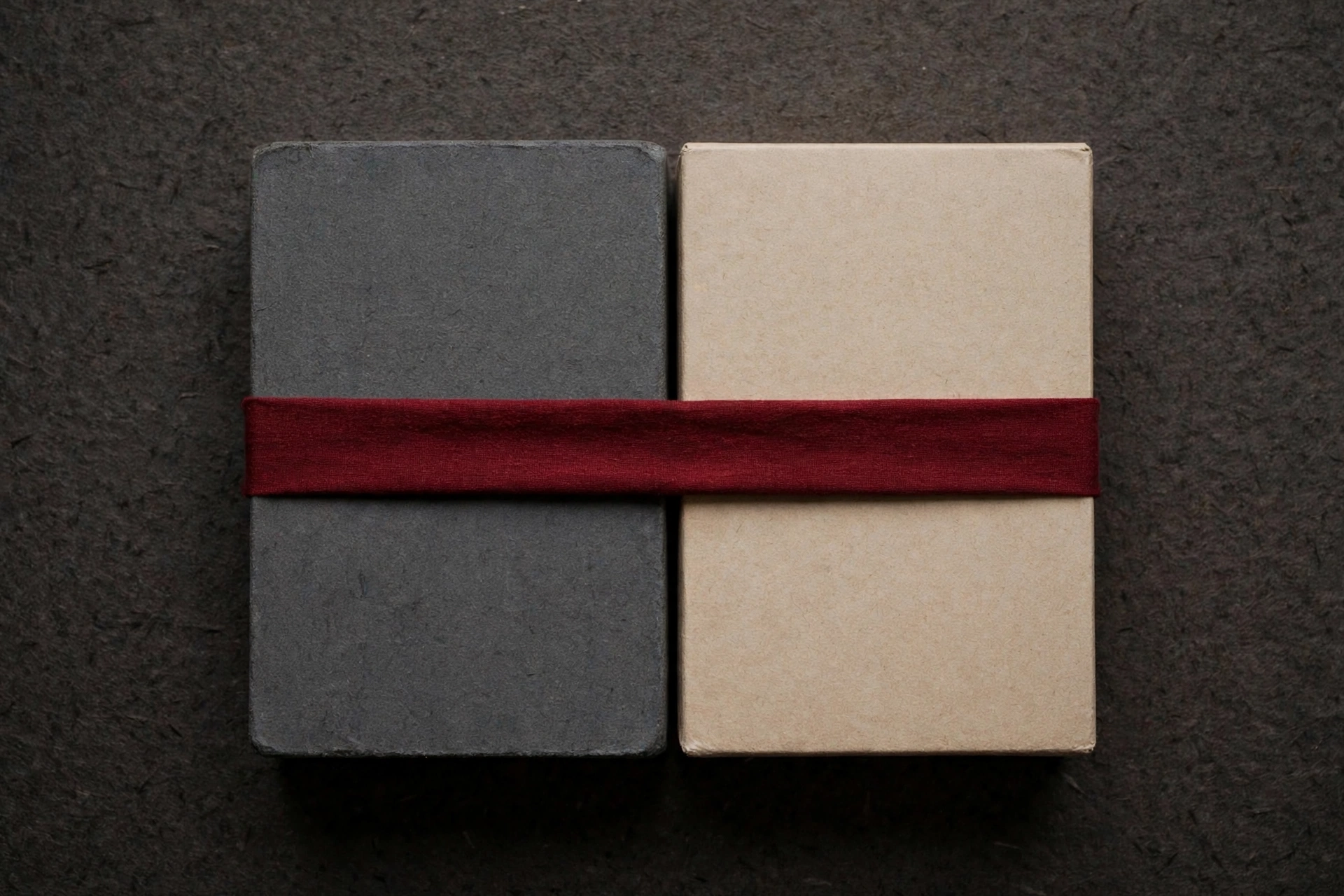 A photograph shows two rectangular boxes, one dark gray and one light tan, joined together and wrapped with a dark red band.